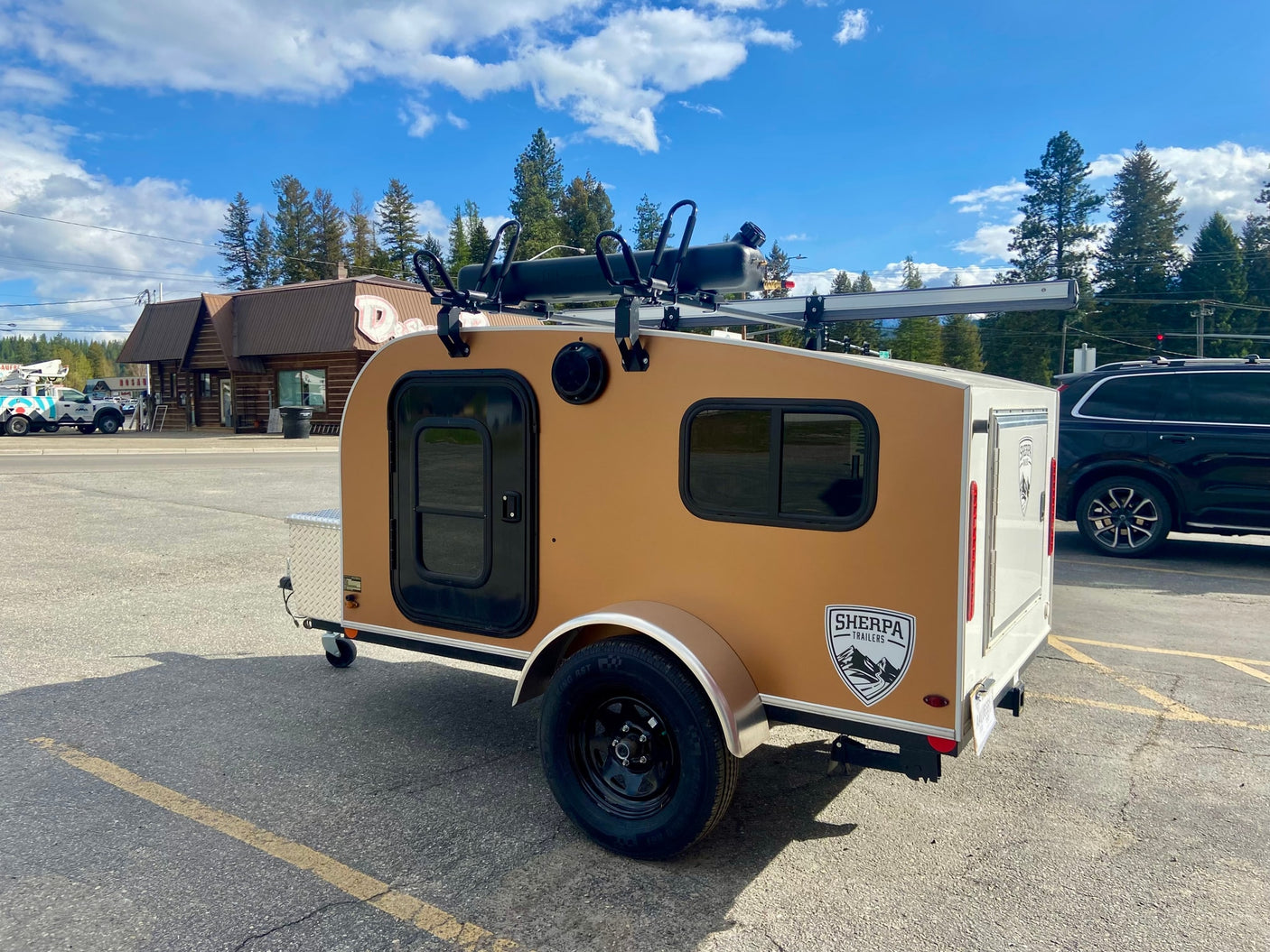 Sherpa Teardrop RV rental: a compact, tan & white camper with roof rack, parked on asphalt under a blue sky.