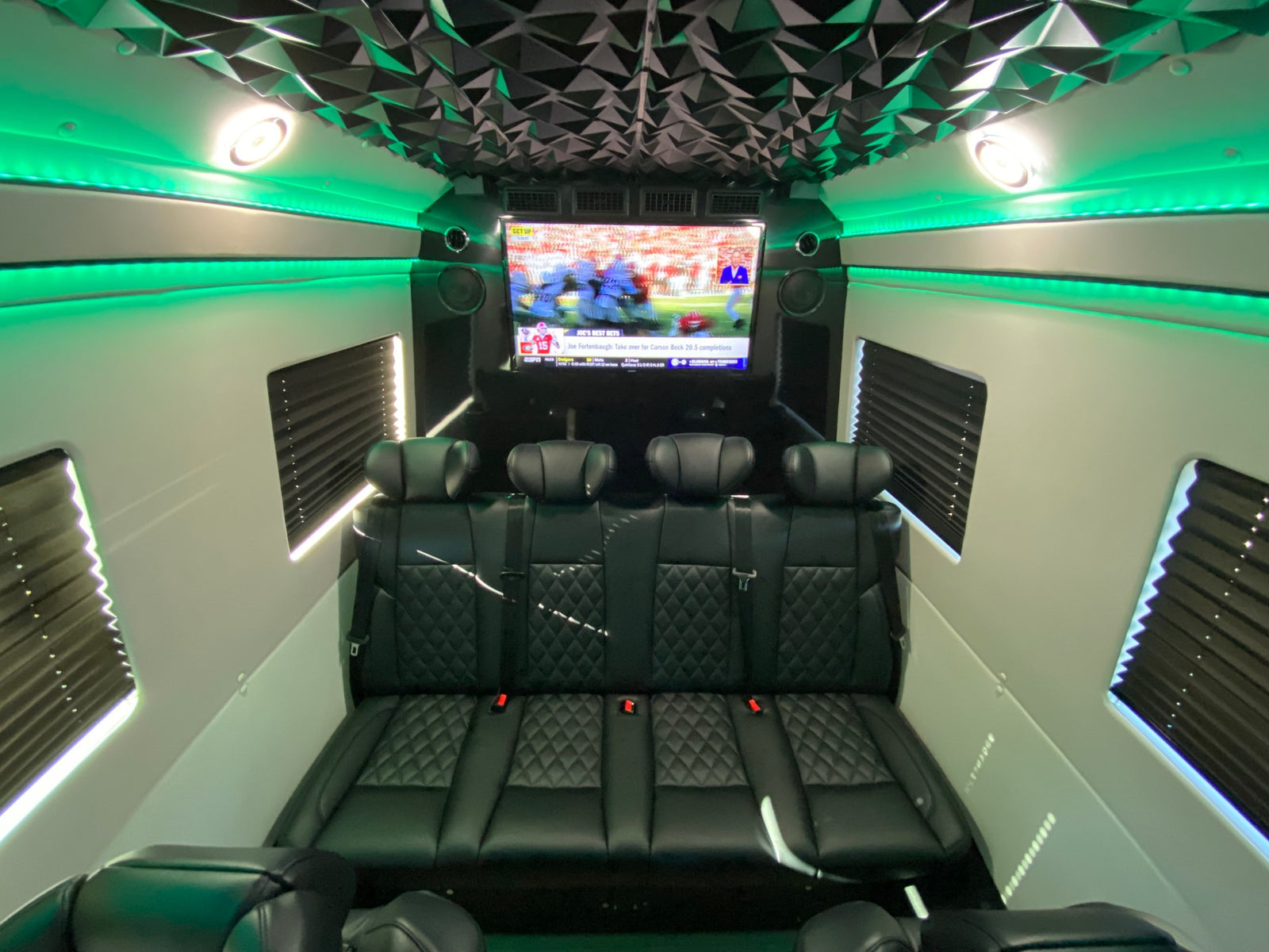 RV rental with custom interior: geometric ceiling, green LED lighting, big TV showing sports, and quilted black leather seats.