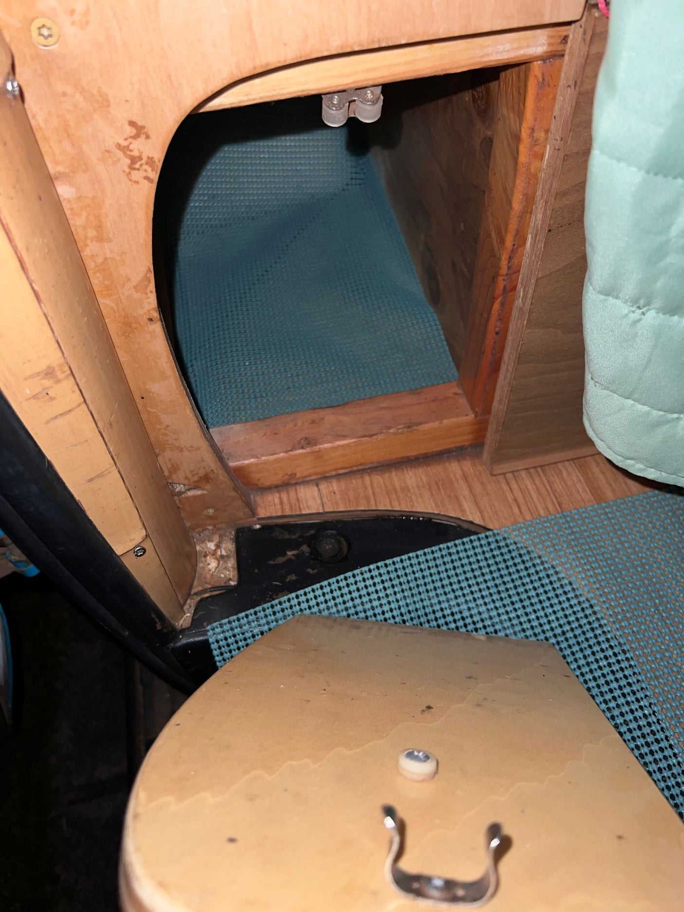 RV rental interior: A wooden cabinet opening reveals storage with a teal mat, part of a cozy camper layout.