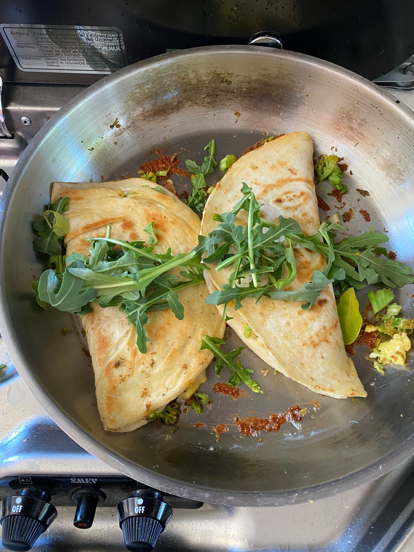 Quesadillas with arugula in a pan on an RV rental stove, ready for a camp meal.