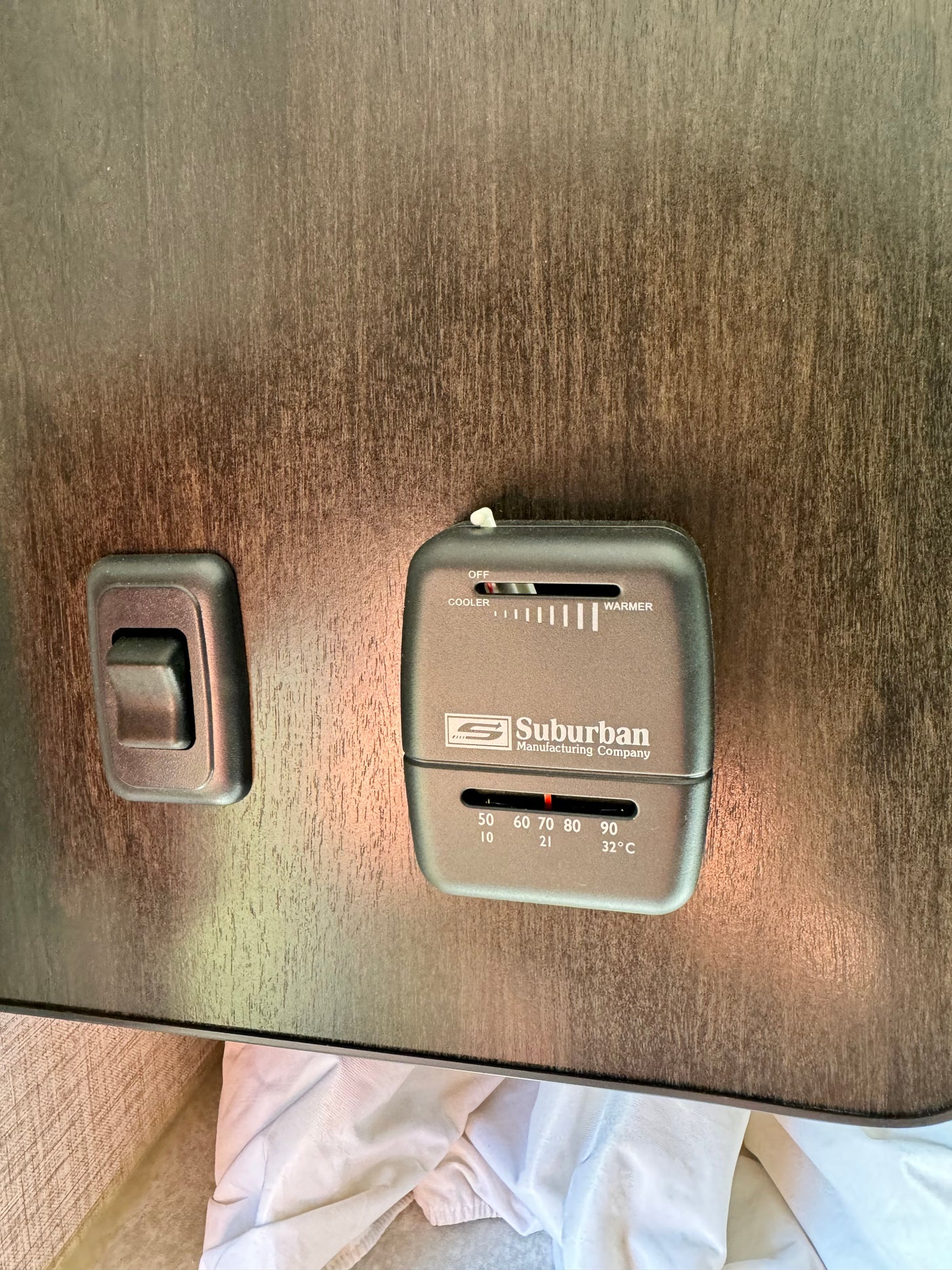 Suburban RV thermostat and light switch on wood panel wall, set to 70°F/21°C. Essential for rv rental climate control.