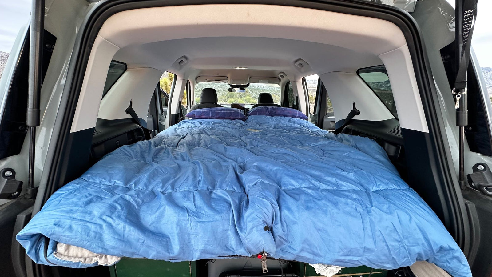showing map and menu. Dash controls below. Ready for an RV rental trip.|View inside SUV: cargo area converted into a bed with blue sleeping bag and pillows. Car camping comfort