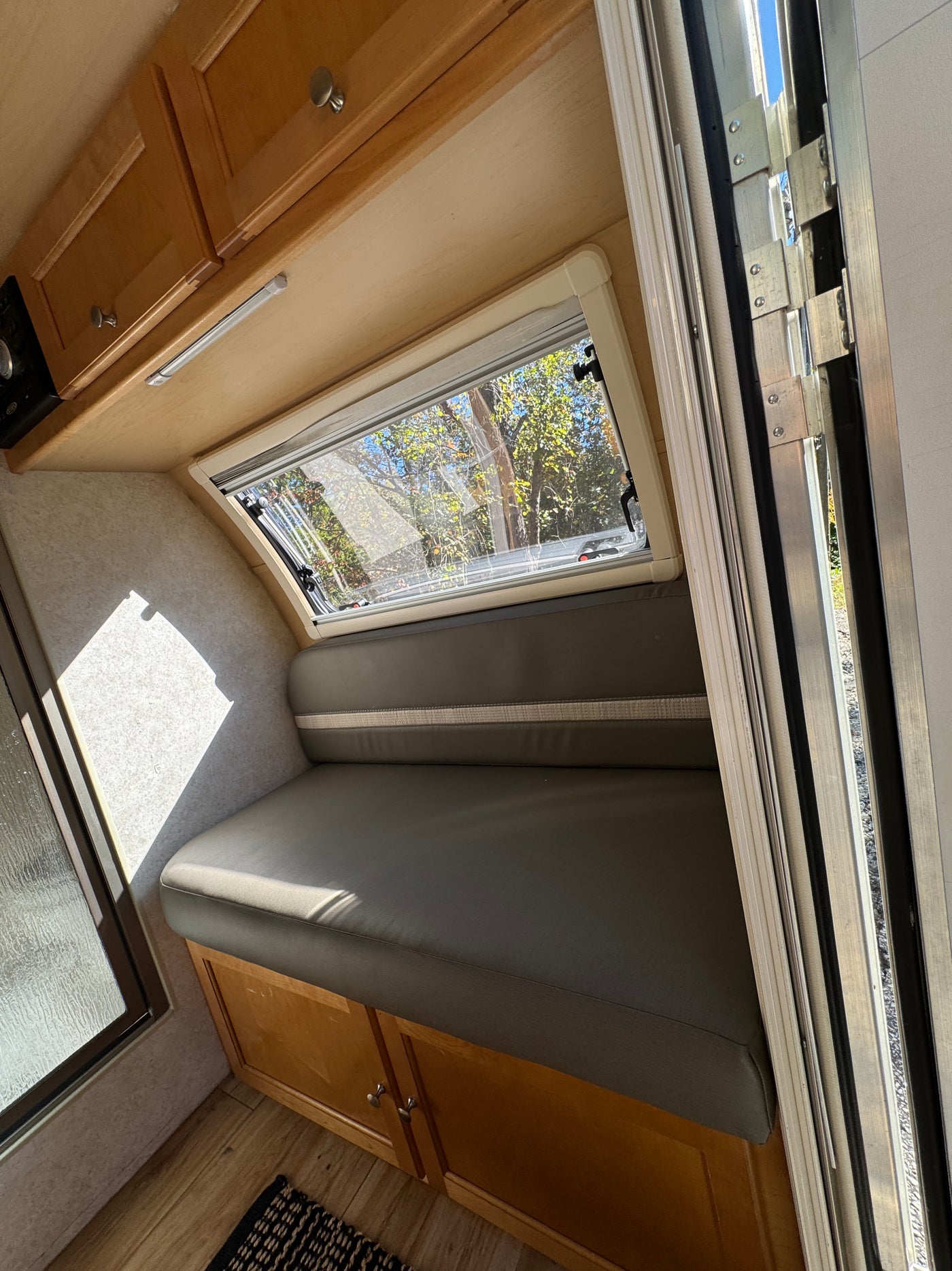 Bright RV rental interior: gray bench seating, wooden cabinets, and window with an outdoor tree view. — photo 13