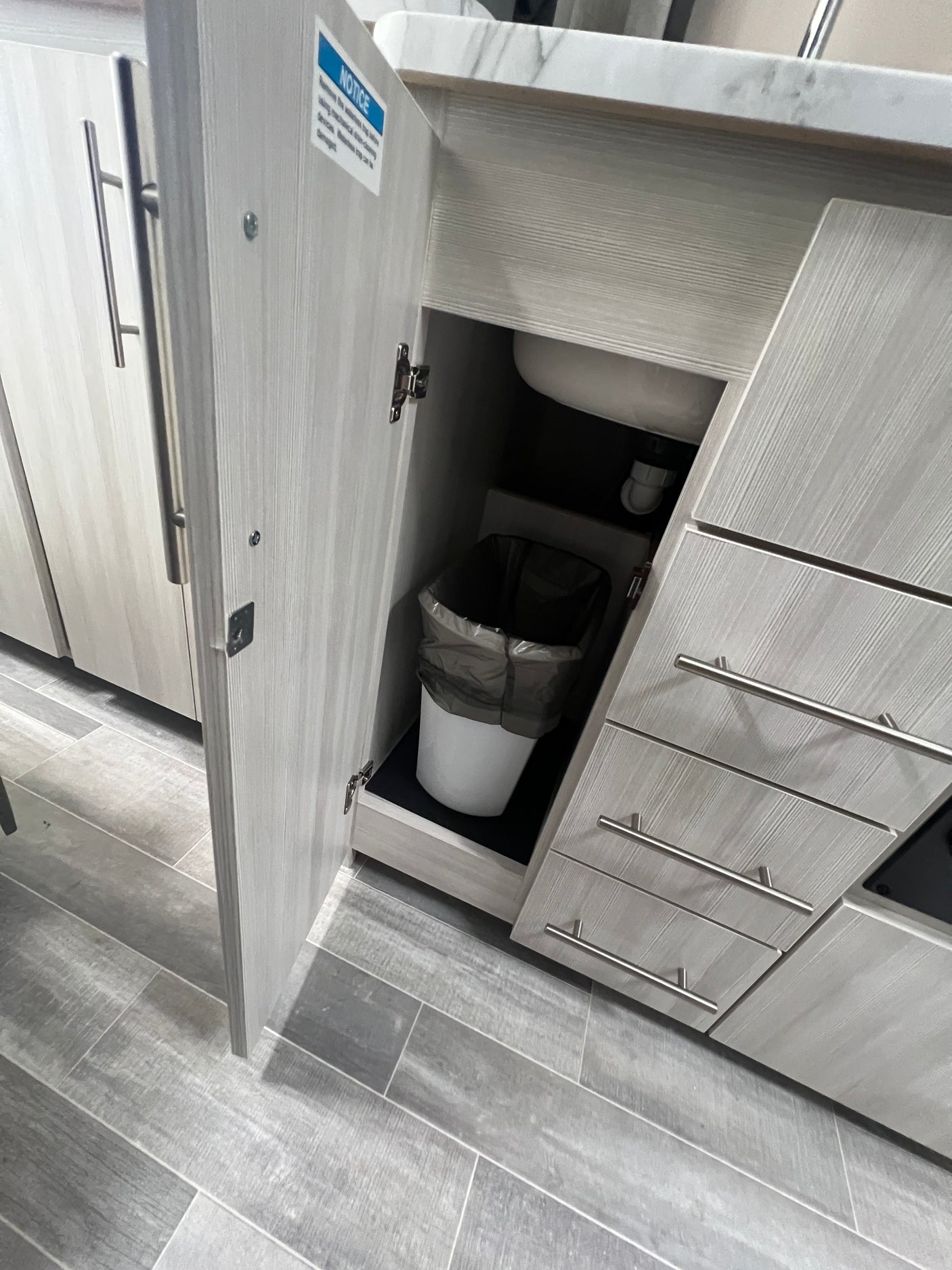 Efficient **RV rental** kitchen with under-sink trash, drawers & light wood cabinets on a tiled floor.