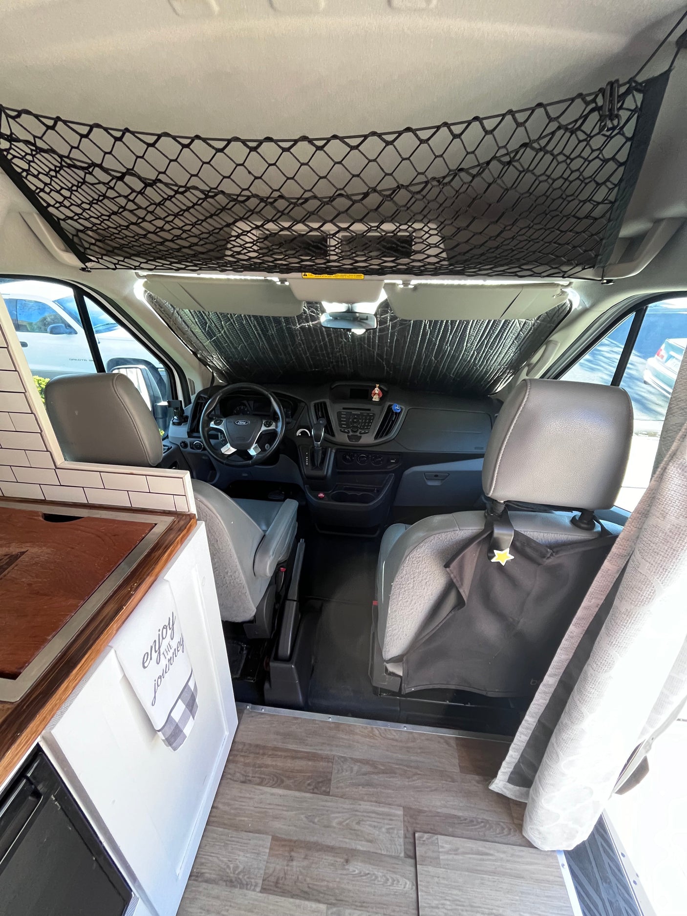 Inside this RV rental camper van: a neat cockpit with sunshade, overhead net, and a compact kitchen. Ready for adventure!