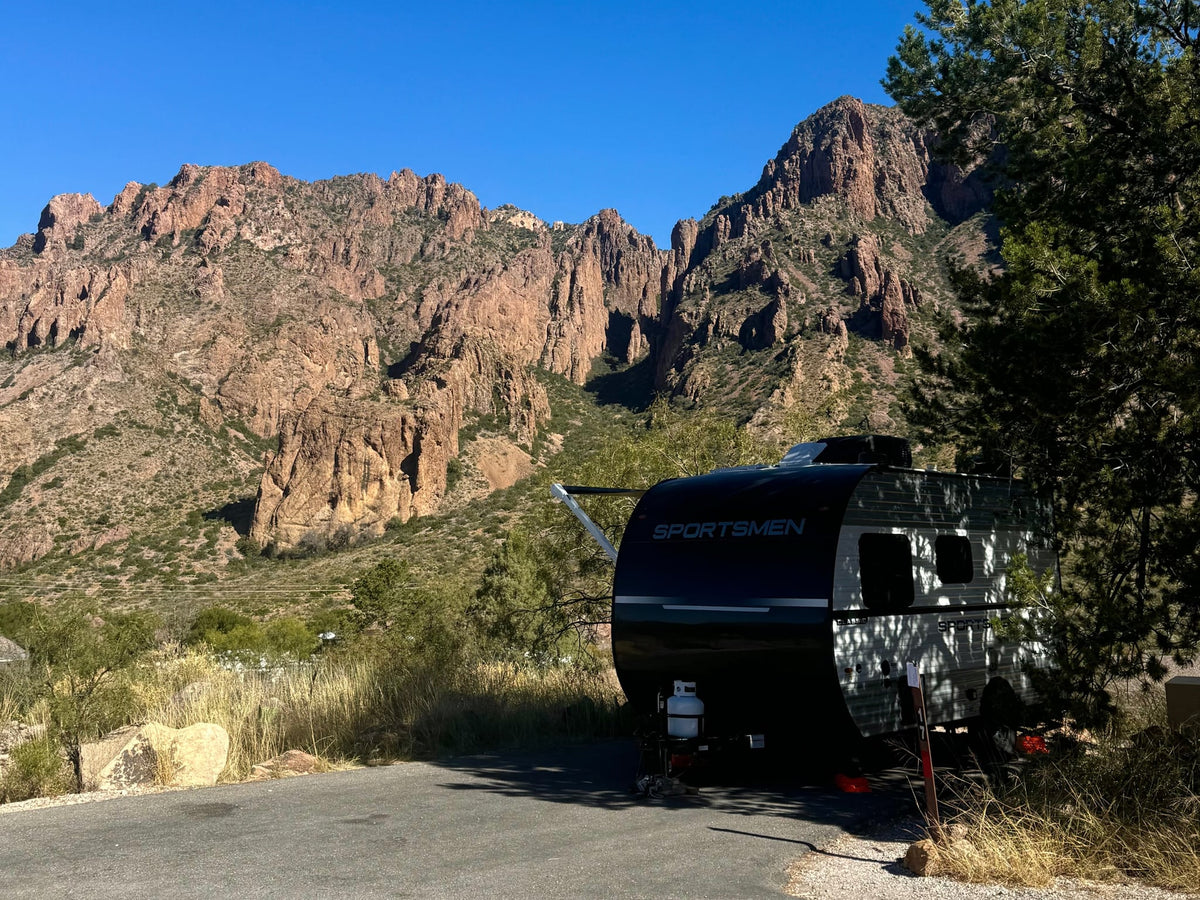 hitched to a pickup truck at a serene campsite.|Rugged mountains backdrop this rv rental travel trailer parked at a scenic campsite. Enjoy desert camping!||Inside a modern RV rental bedroom featuring a striped bed — photo 2
