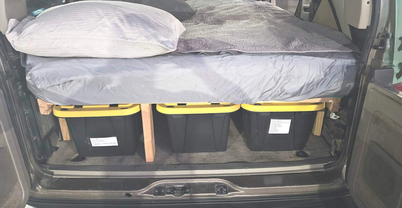 Custom vehicle camping bed with under-bed storage using three yellow-lidded bins. A clever RV rental alternative for road trips.