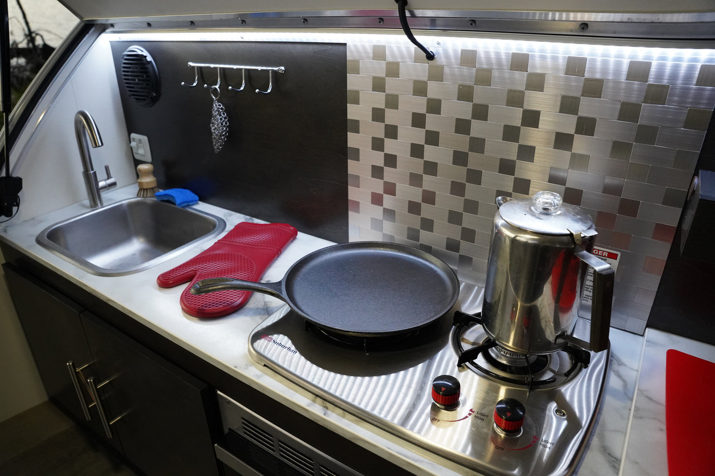 Enjoy home comforts in this RV rental's compact kitchen. Features a sink, stove, pan, and percolator.