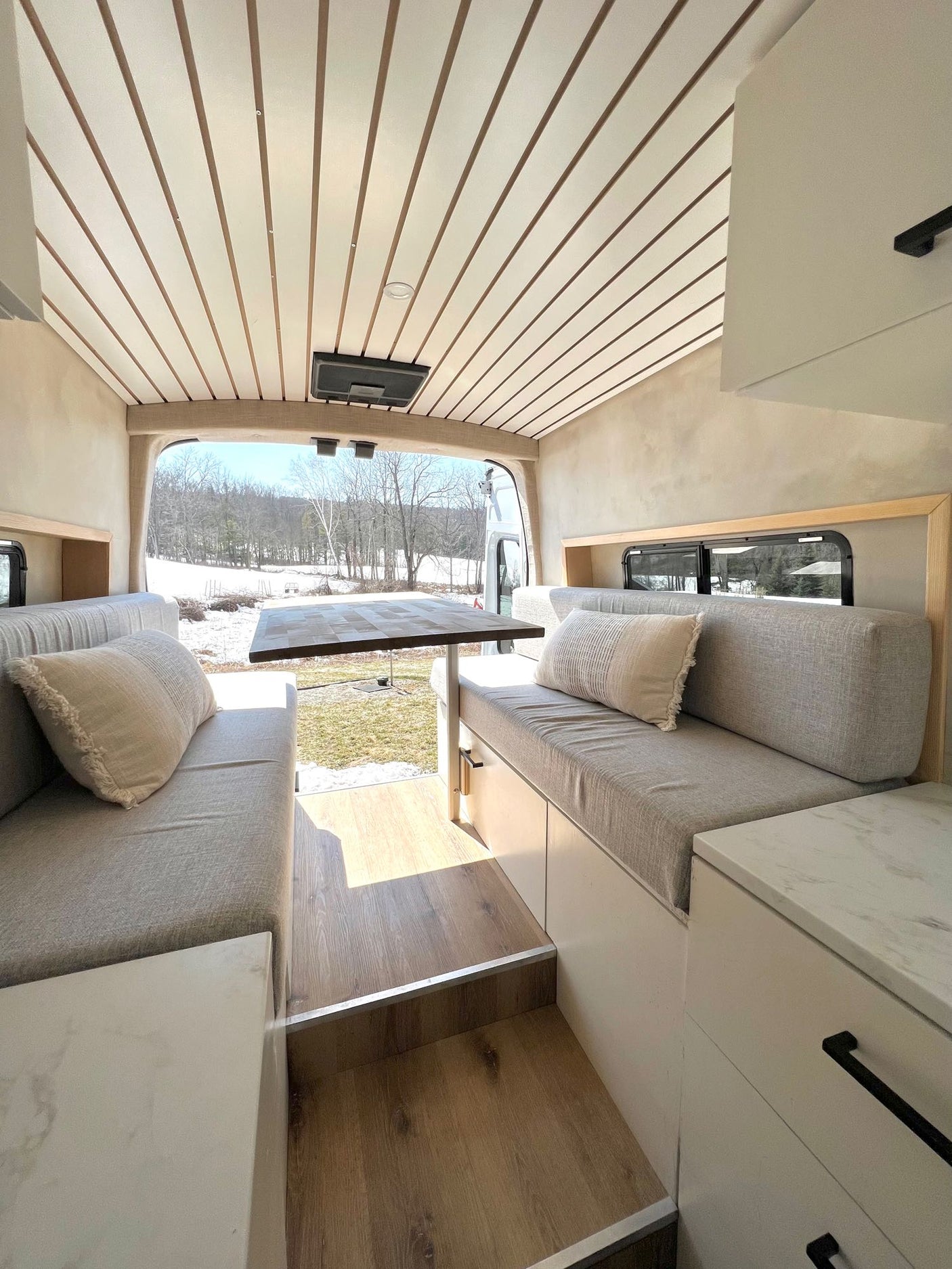 Cozy RV rental interior with comfortable seating, dining table, and scenic winter outdoor view. Ideal mobile living space.