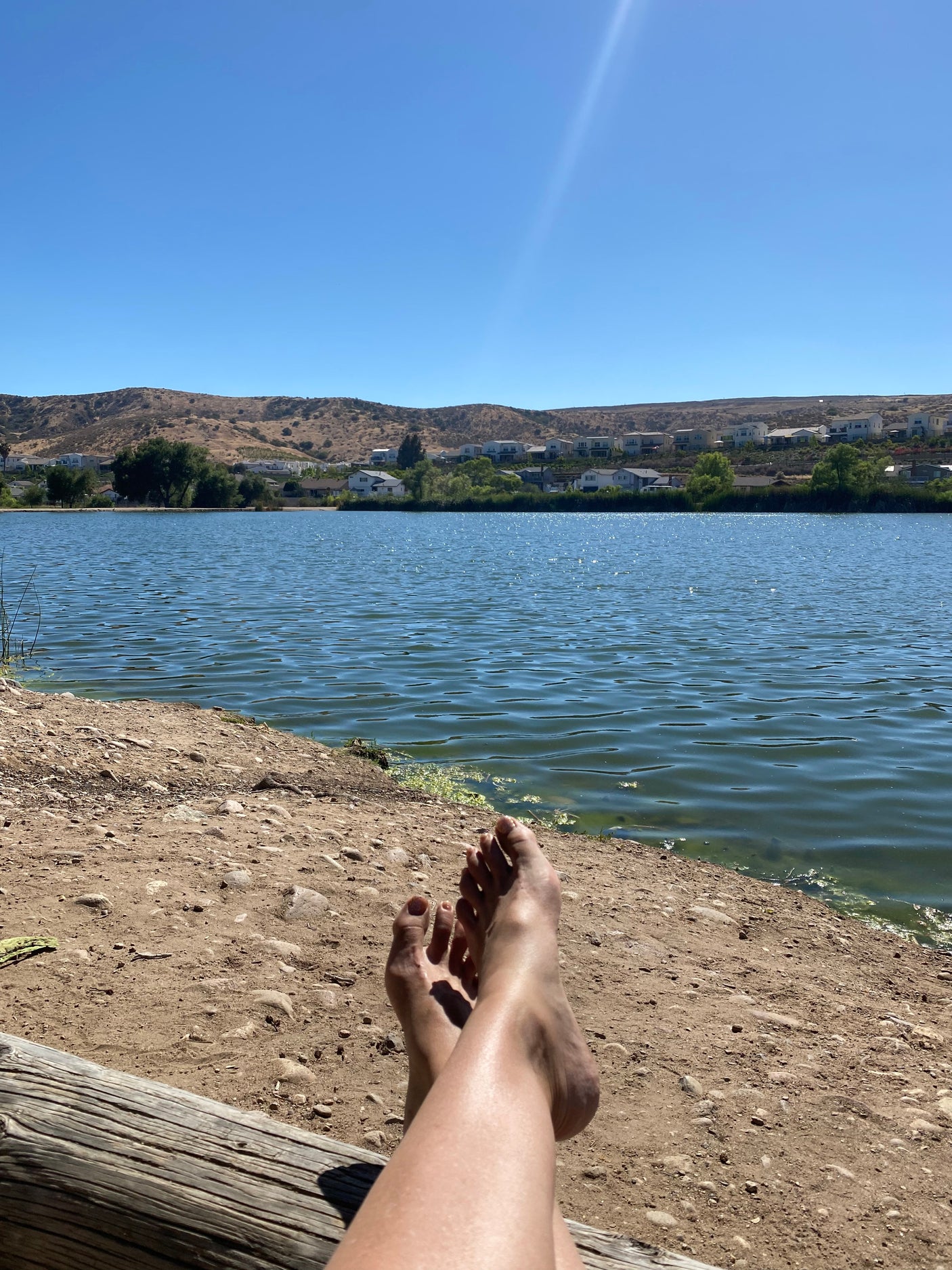 Relaxing view: bare feet propped on a log, serene lake, hills & houses. Perfect for an rv rental getaway.