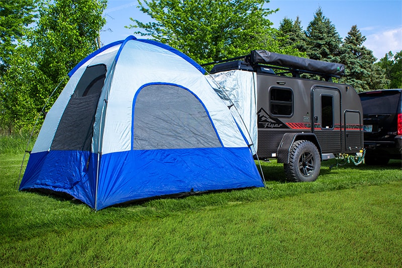 Large blue tent attached to a compact gray 'Flyer' travel trailer, ideal for an RV rental adventure in nature.