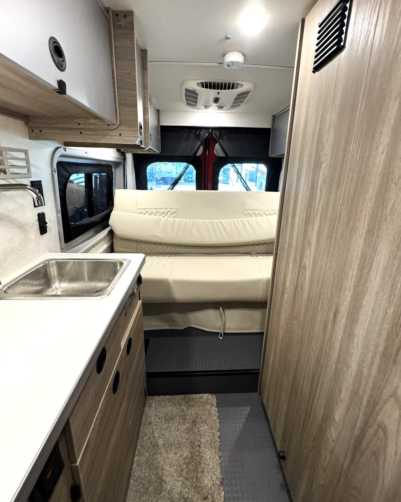 RV rental: a small camper van interior with a kitchen sink on the left, comfortable bed, and wood-toned cabinets.