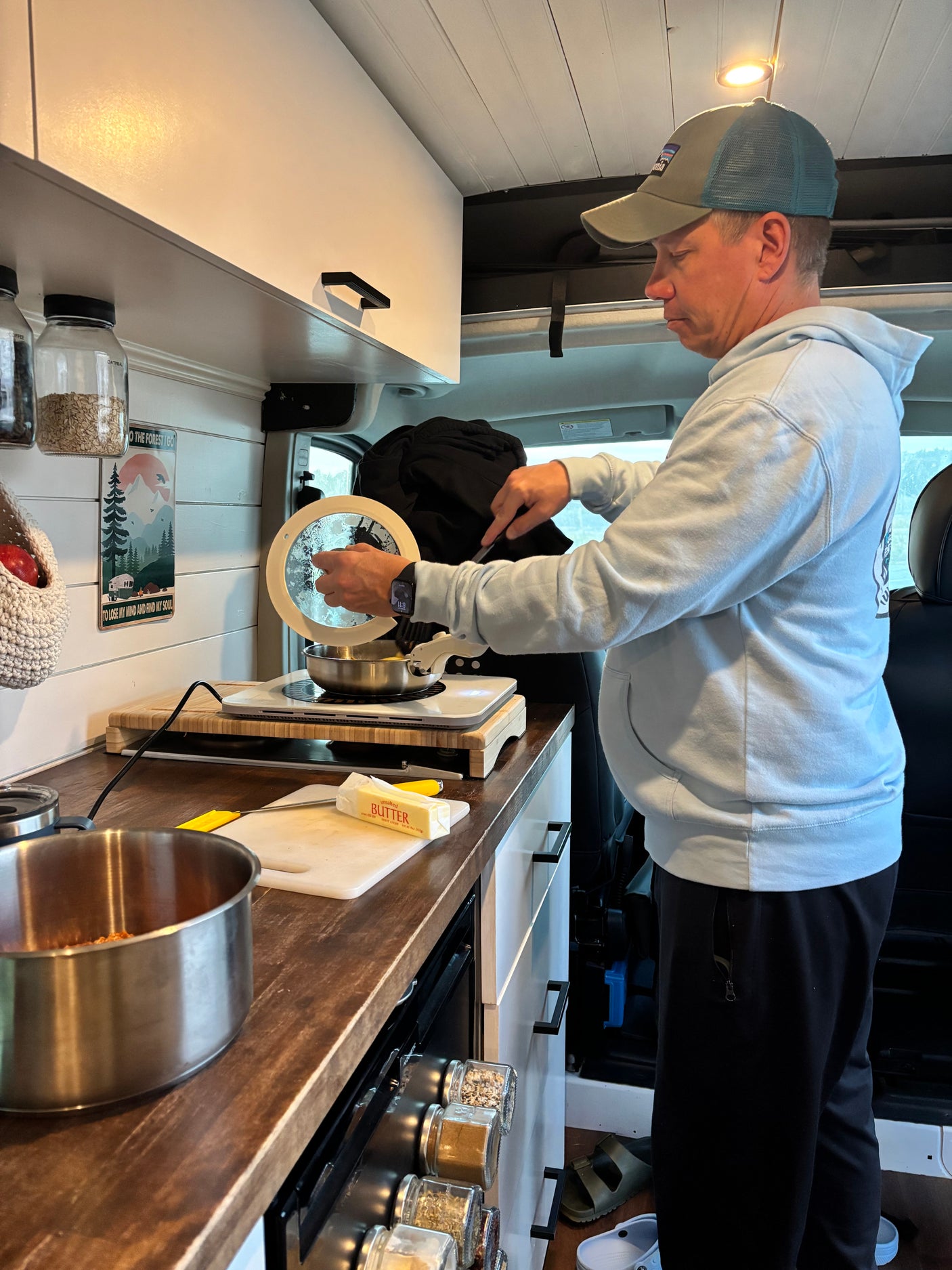 RV rental cooking: A man preps a meal in a compact, organized kitchen, featuring butter, spices, and travel decor.