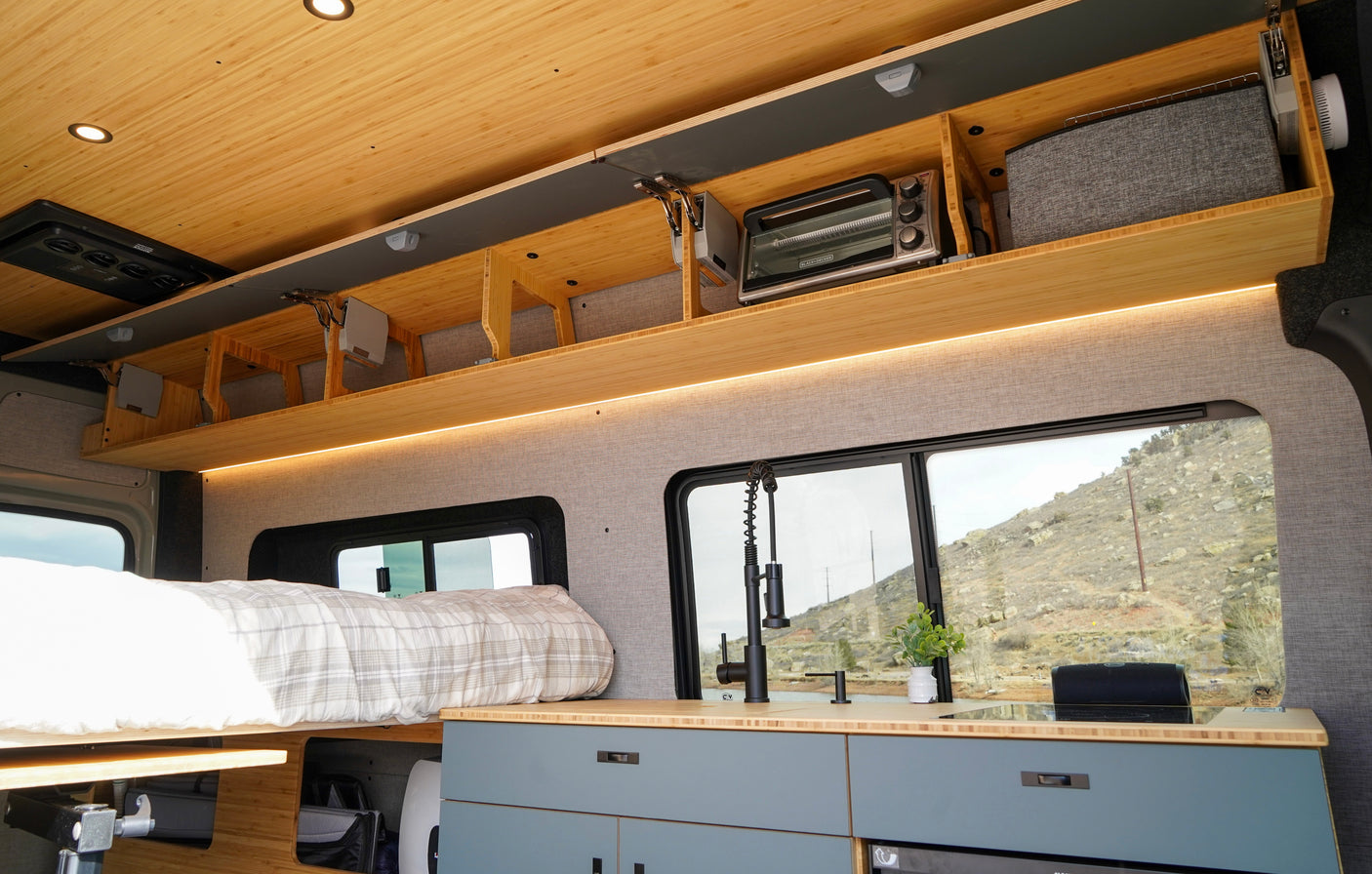 RV rental camper interior with bed, compact kitchen, toaster oven, and organized overhead storage, plus scenic window views.