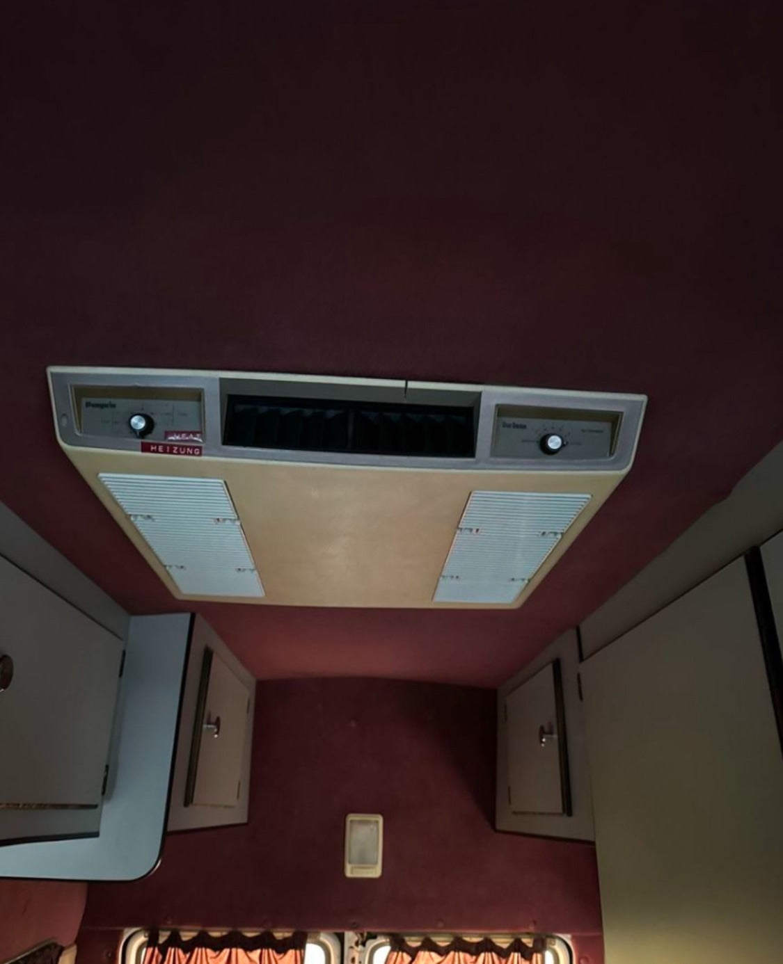 RV rental interior: ceiling-mounted HVAC unit with 'HEIZUNG' controls, vents, and storage cabinets.