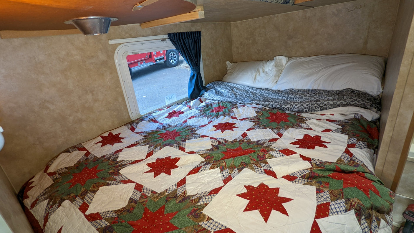 Cozy RV rental bedroom with a colorful star quilt and pillows, offering a comfortable sleeping space with a window view.
