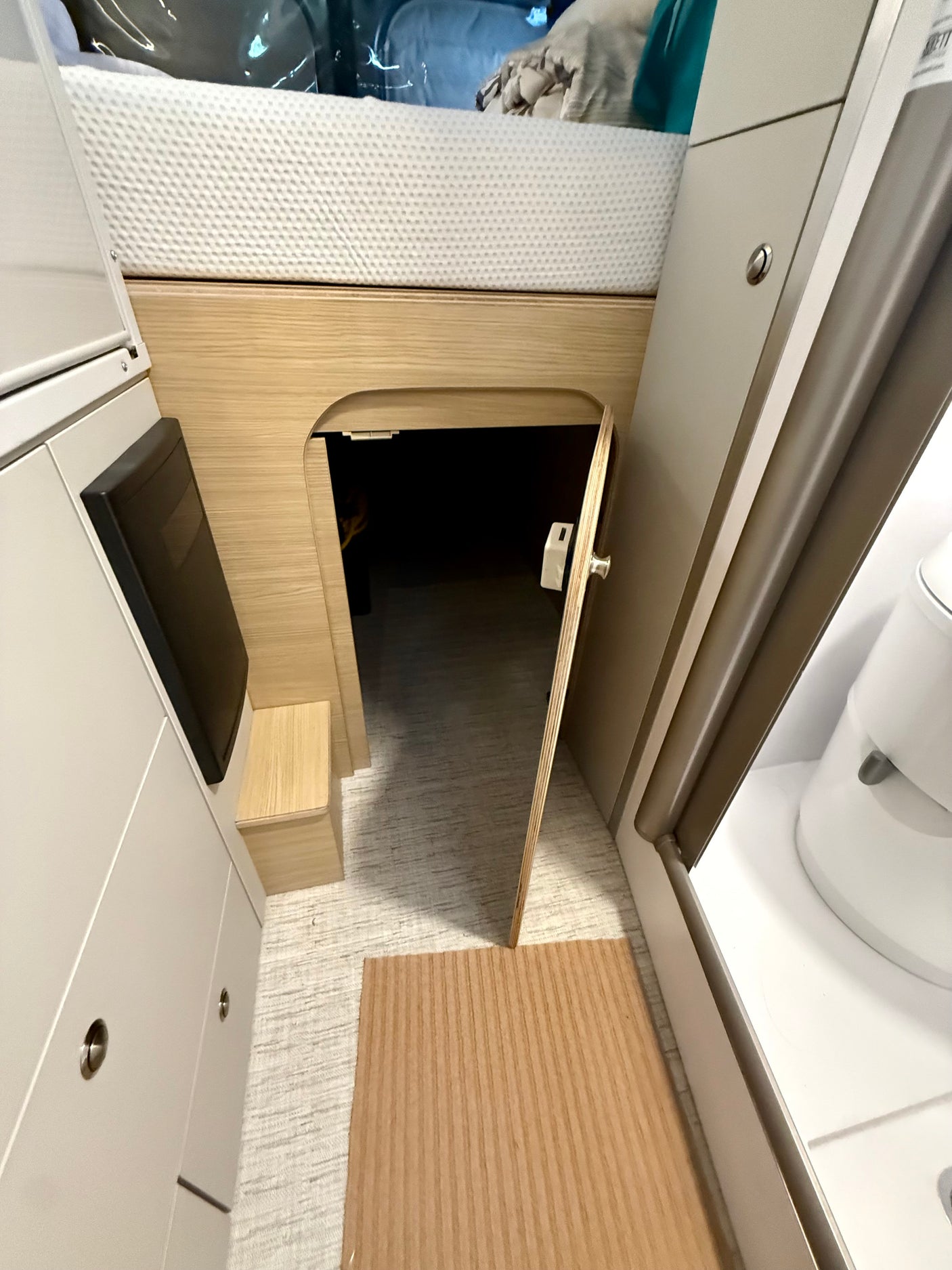 RV rental interior: View of an overhead bed, under-bed storage access, and a peek into the compact bathroom.