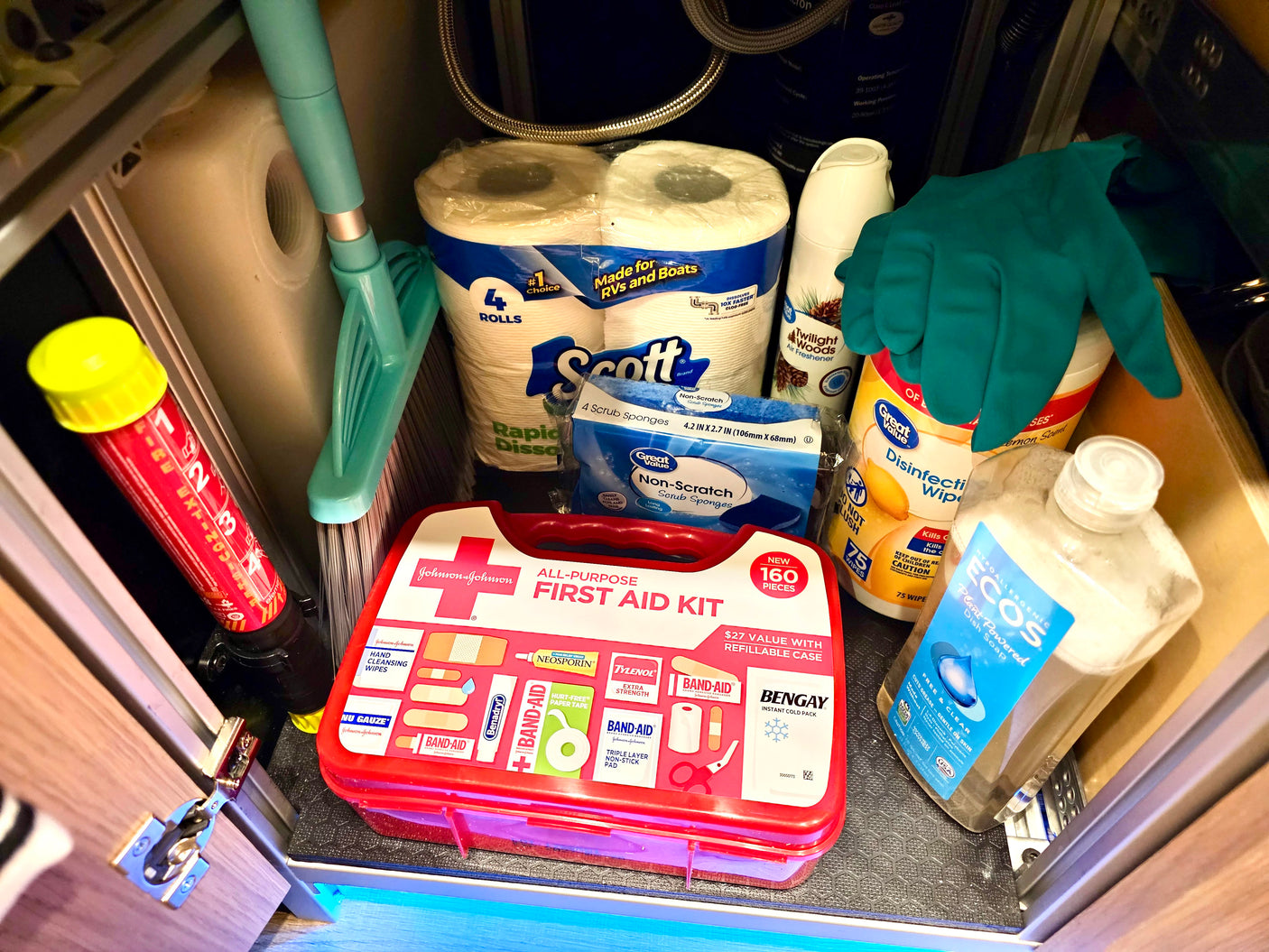 Compact RV rental storage: first aid kit, fire extinguisher, cleaning supplies, and RV-specific toilet paper for travel.