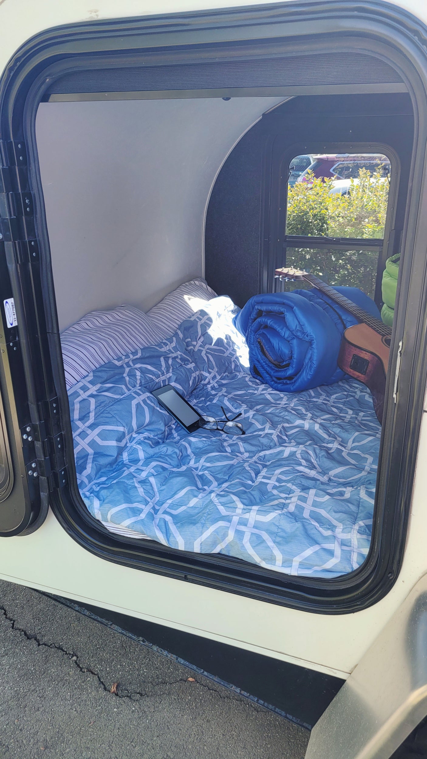 Cozy RV rental interior with a bed, blue bedding, phone, glasses, guitar, & rolled sleeping bag. Ready for adventure!