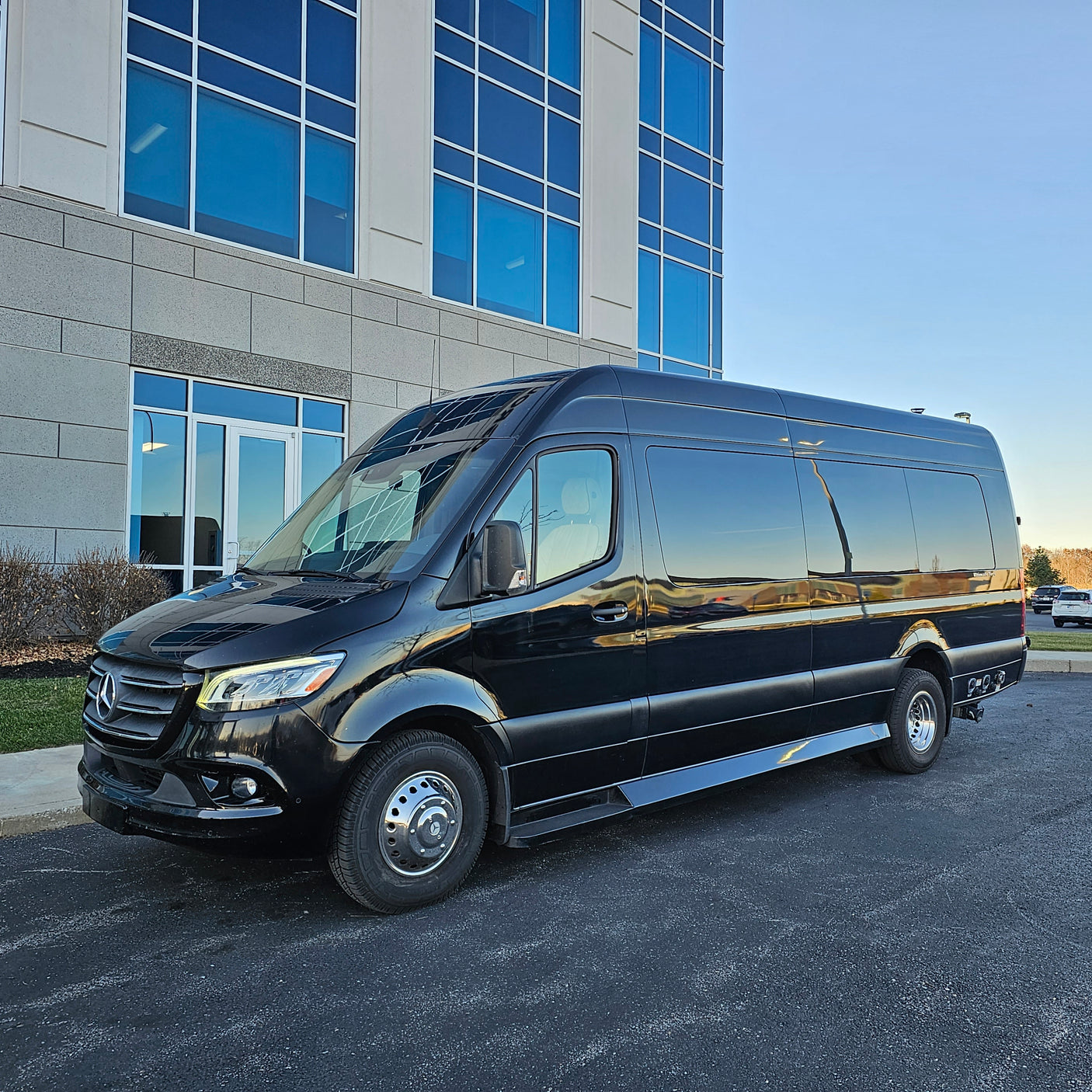 This elegant black Mercedes-Benz Sprinter van is a fantastic RV rental choice, parked in front of a sleek blue-windowed building.