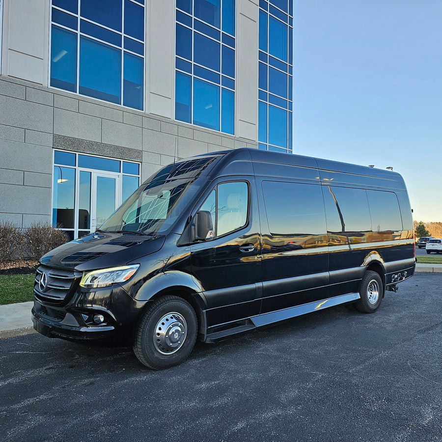 This elegant black Mercedes-Benz Sprinter van is a fantastic RV rental choice, parked in front of a sleek blue-windowed building.