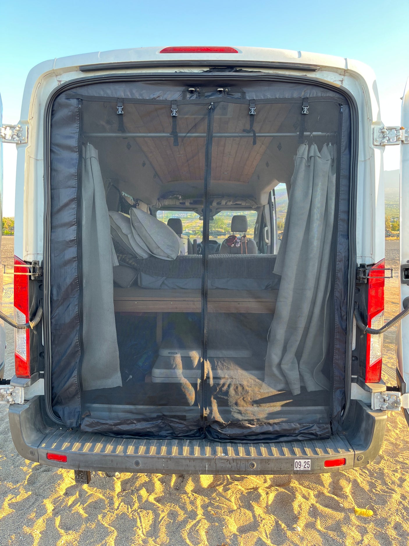 Inside an RV rental van, a rear mesh screen provides bug protection. Features include a bed and storage for comfortable travel.
