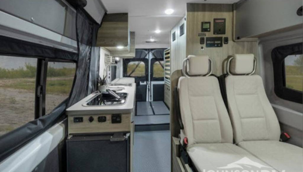 View of an RV rental interior: compact kitchen, two passenger seats, and control panels. Ready for adventure.
