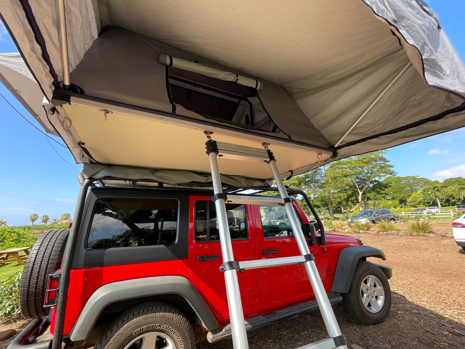 Red Jeep Wrangler with an open rooftop tent & ladder, a unique rv rental for your outdoor camping trip.