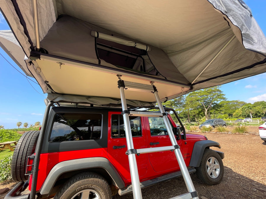 Red Jeep Wrangler with an open rooftop tent & ladder, a unique rv rental for your outdoor camping trip.