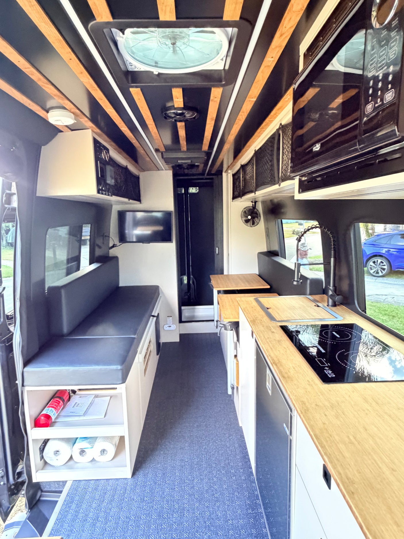 RV rental interior: modern camper van with wood-slatted ceiling, kitchenette, bench seating, microwave, and storage.