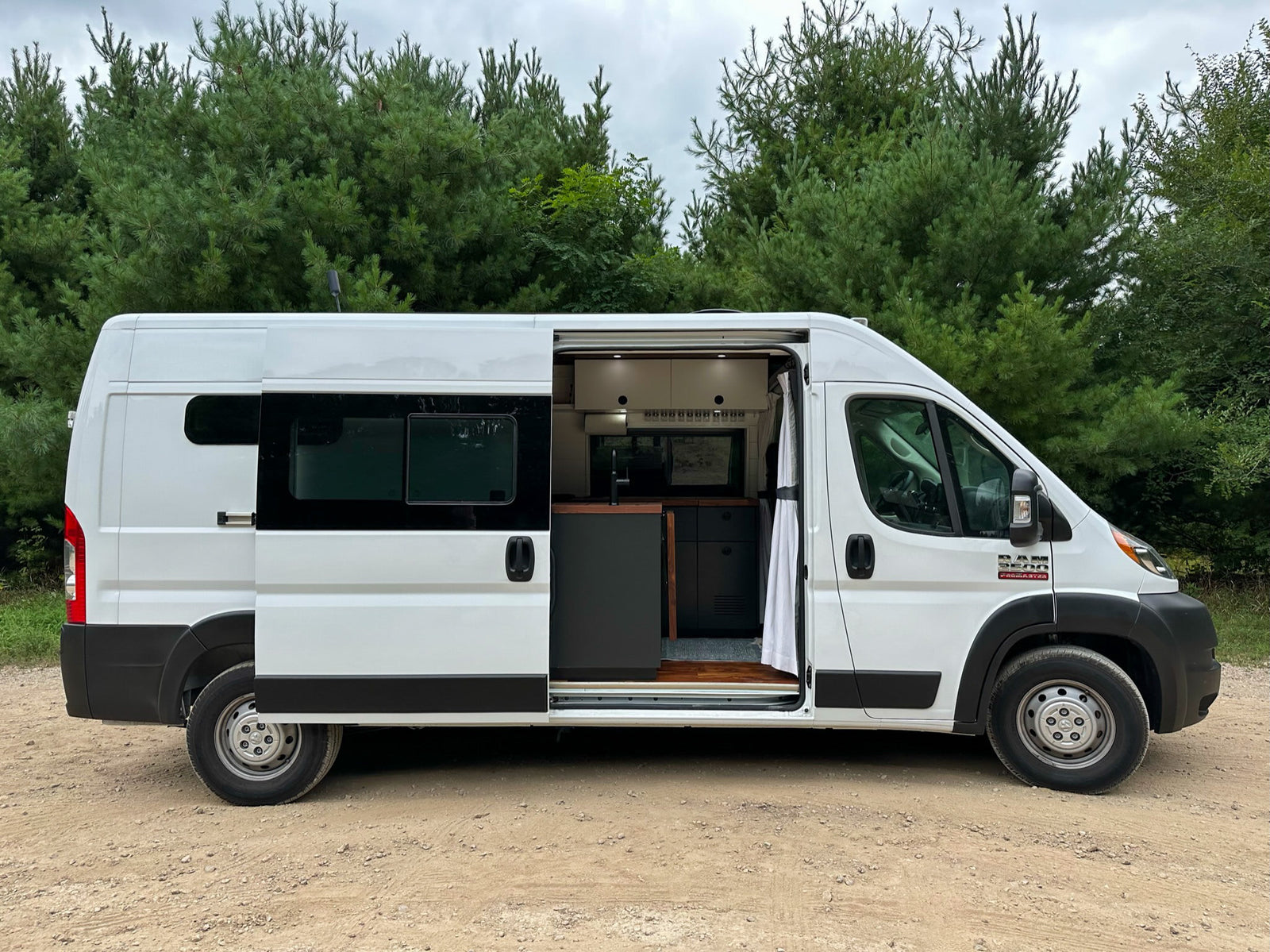 surrounded by unique eroded landscapes under a cloudy sky.|White Ram ProMaster rv rental van with side door open