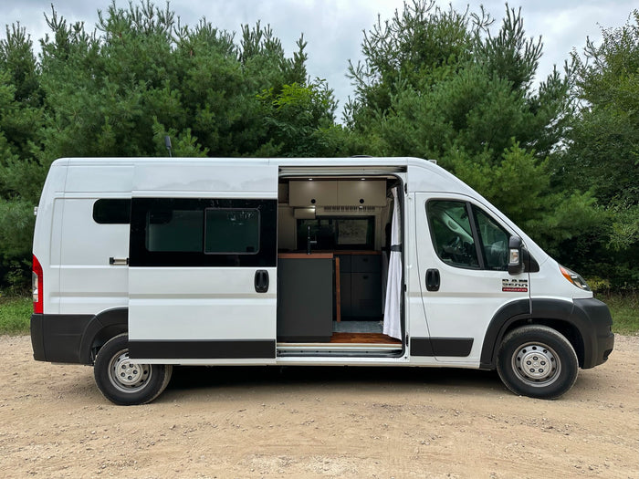 surrounded by unique eroded landscapes under a cloudy sky.|White Ram ProMaster rv rental van with side door open