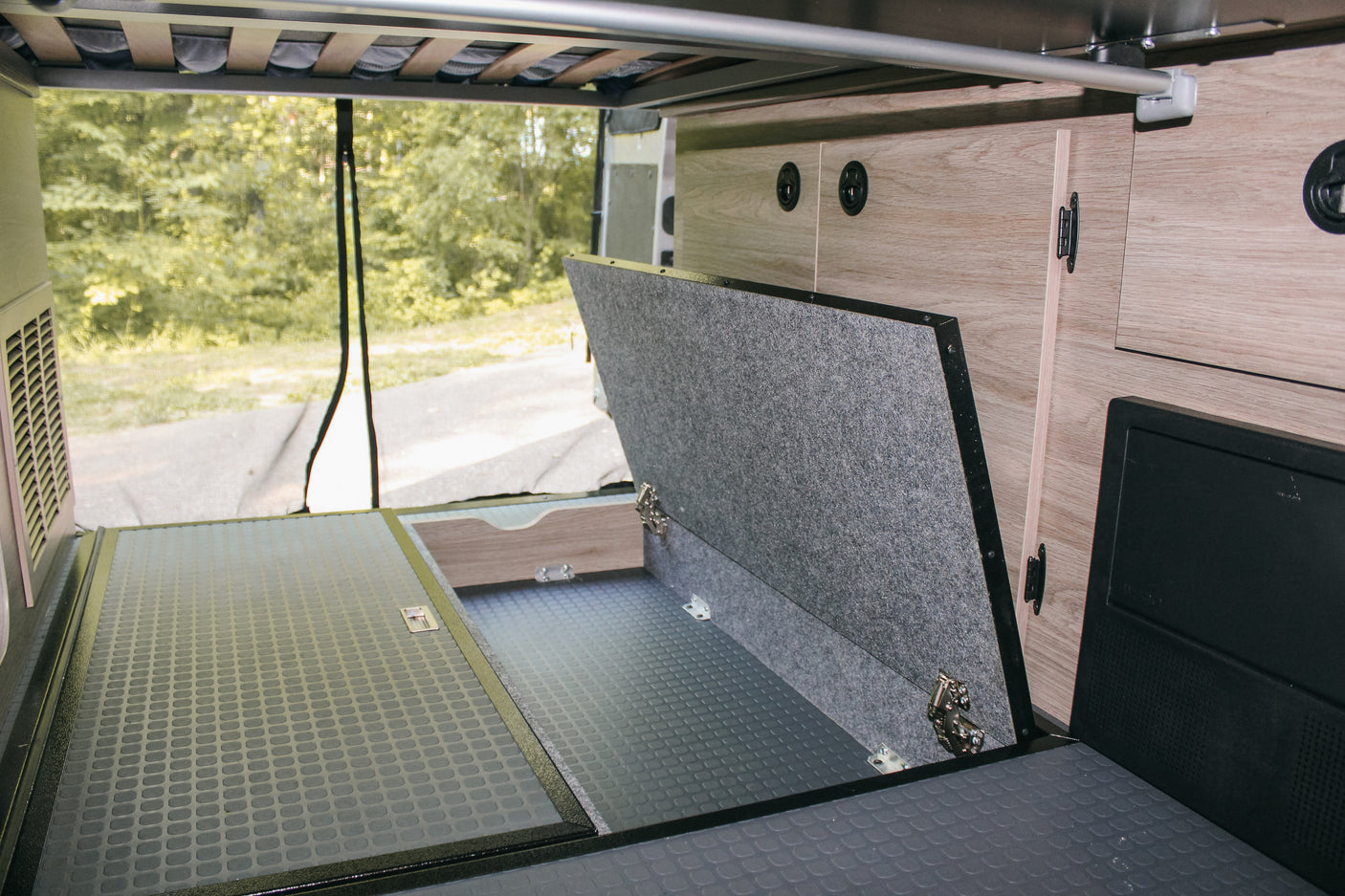 RV rental: Organized rear storage with lift-up floor, rubberized mat, and wood cabinets. Bed frame visible overhead.