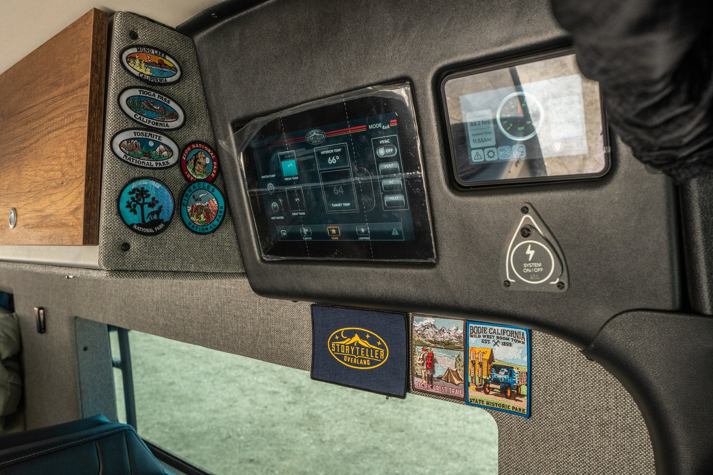RV rental interior featuring system controls for water & climate (66°F), with national park & adventure patches on fabric walls.