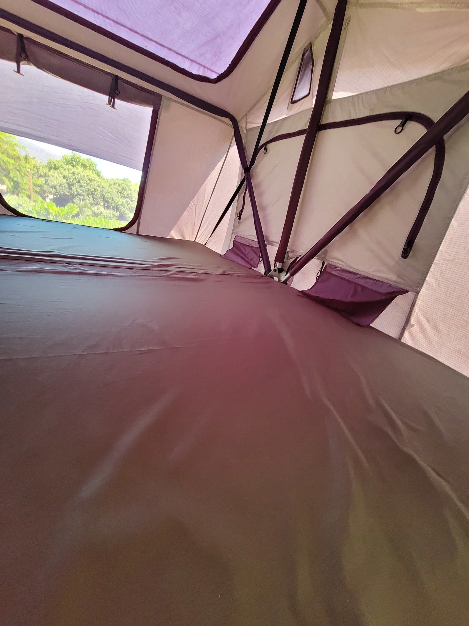 RV rental adventure: Interior of a spacious rooftop tent with a comfortable mattress and scenic outdoor view.