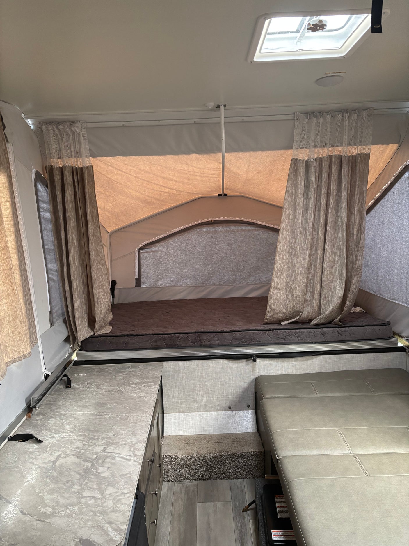 Inside an RV rental pop-up camper, featuring a cozy bed, patterned curtains, sleek counter, and plush seating.