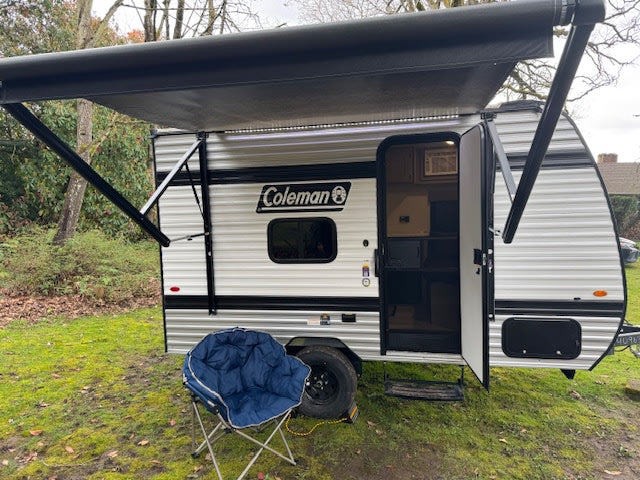 This Coleman travel trailer with an extended awning and open door is ready for an RV rental adventure. A blue chair sits nearby.|Inside a modern RV rental: compact kitchen with microwave