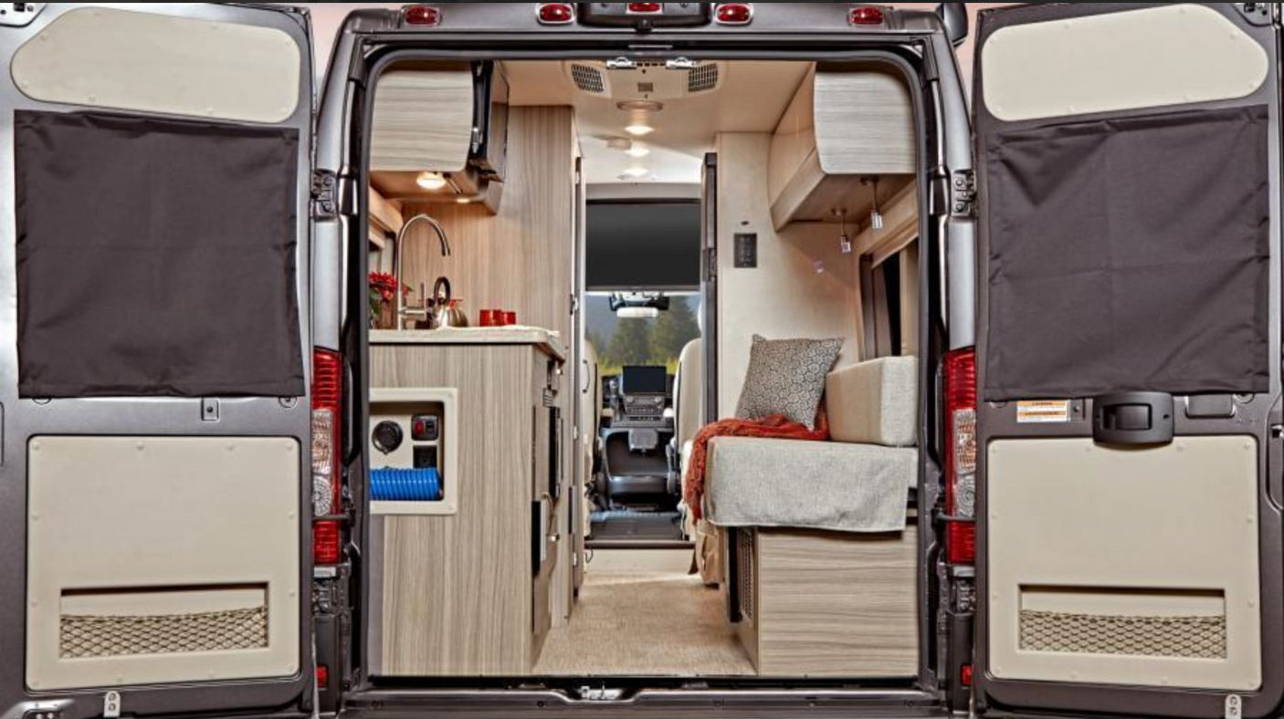 View from rear: an RV rental's inviting interior. Left: functional kitchen. Right: comfortable seating/bed. Doors open to reveal.