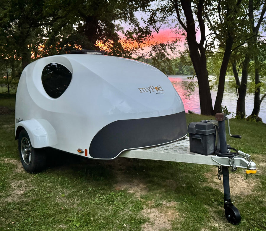 Discover this MyPod teardrop **rv rental**, perfect for scenic camping trips. Parked by a lake reflecting a vibrant sunset.