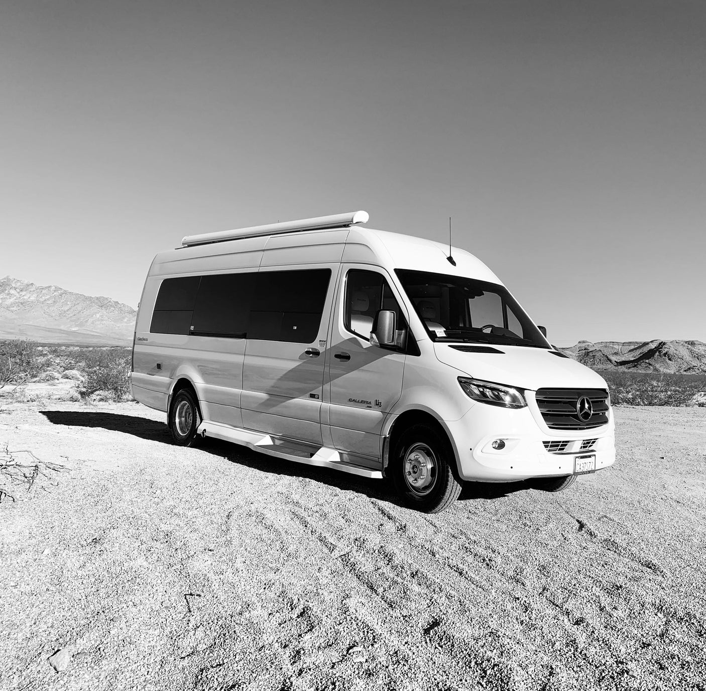 A white Mercedes-Benz Sprinter rv rental parked on a gravel road in a vast desert landscape with distant mountains.