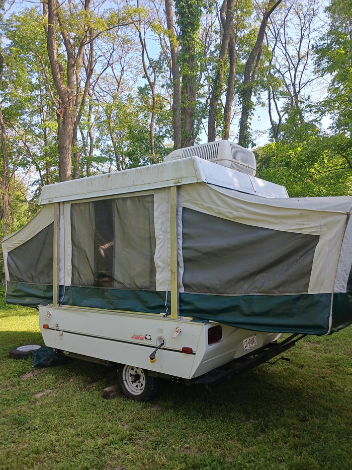 This pop-up camper, ideal for an RV rental, is set up in a wooded campsite, ready for outdoor travel and camping.