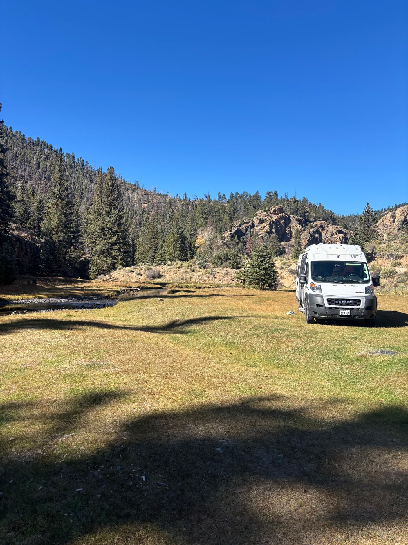 **RV rental** parked in a scenic mountain valley by a stream with pine trees and clear blue skies.