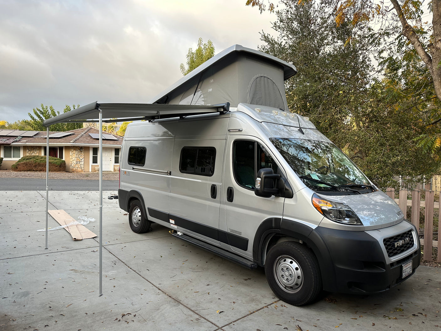 Silver camper van RV rental with a pop-top and extended awning, parked on a driveway, ready for adventure.