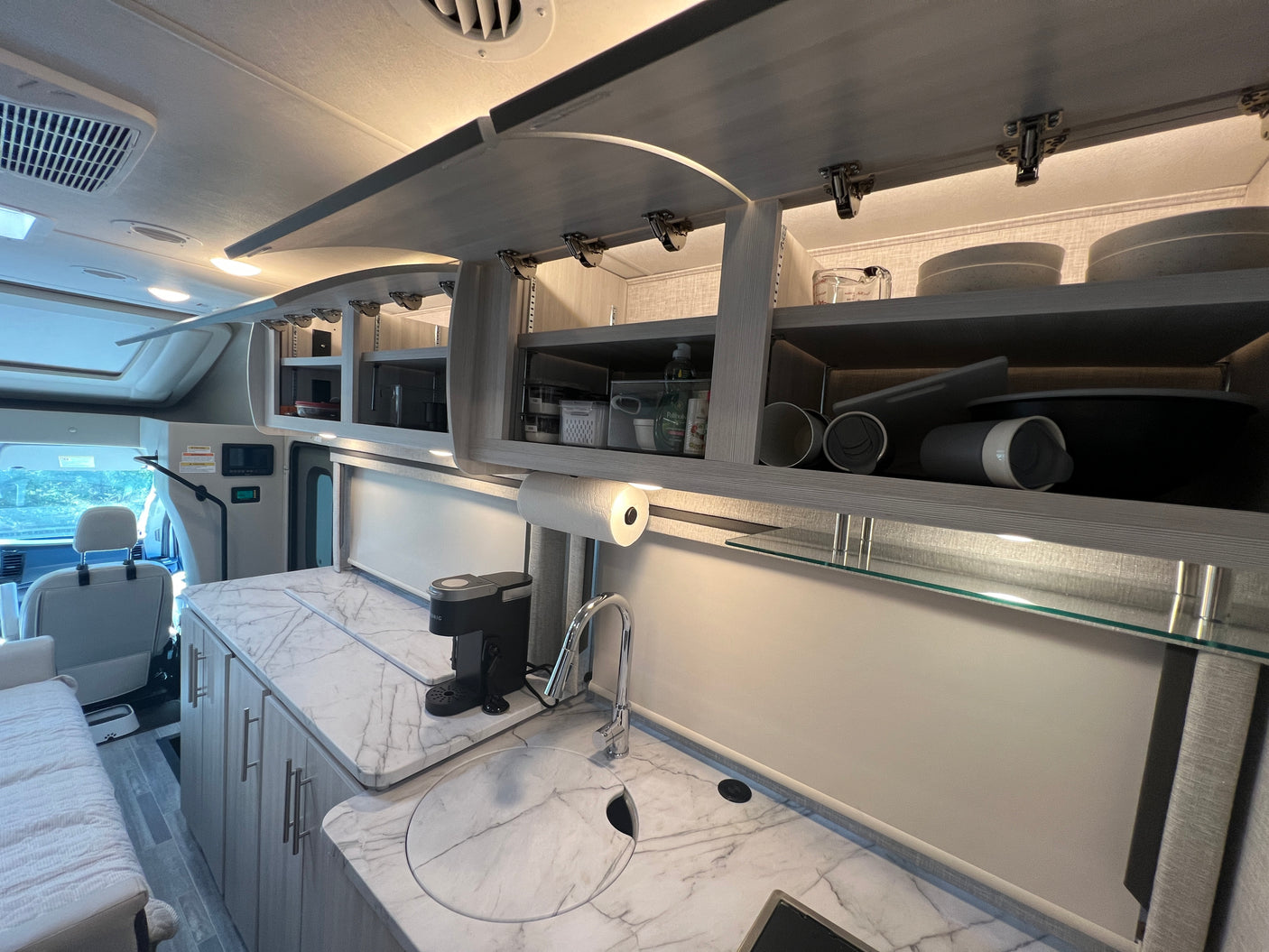 Well-organized RV rental kitchen with modern marble-patterned countertops, a sink, coffee maker, and ample overhead storage.