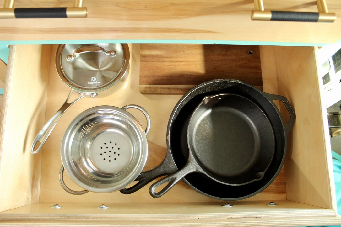 Efficient RV rental kitchen storage: Calphalon pot, colander, and Lodge cast iron skillets neatly organized in a wooden drawer.