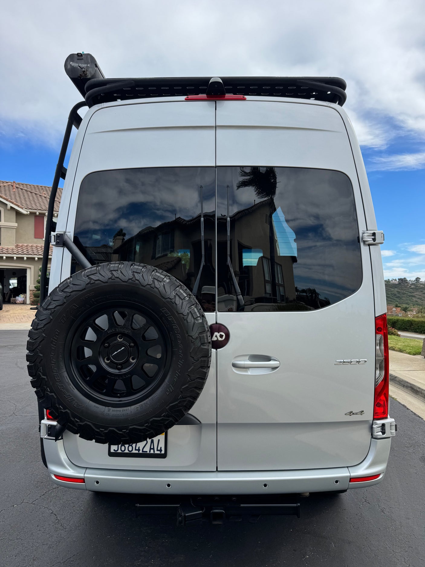 Rear of a custom 4x4 adventure van, perfect for rv rental road trips. Features a roof rack, road shower, and spare tire.