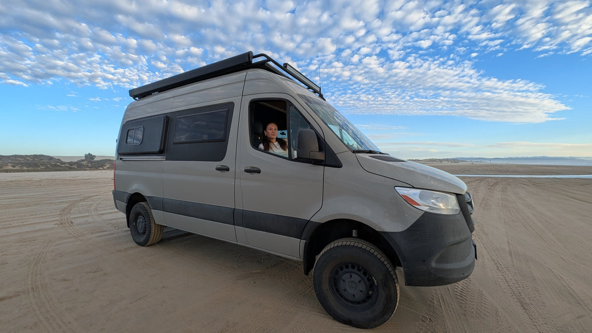 Exploring coastal dunes in an RV rental! A custom camper van on sand, with a woman at the wheel under a cloud-filled sky. — photo 2