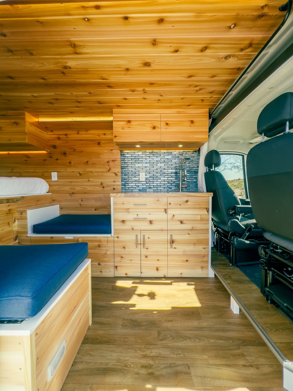 opening to a desert road and mountains. Ideal for road trips.|RV rental: Explore this custom van conversion! Wood-paneled interior