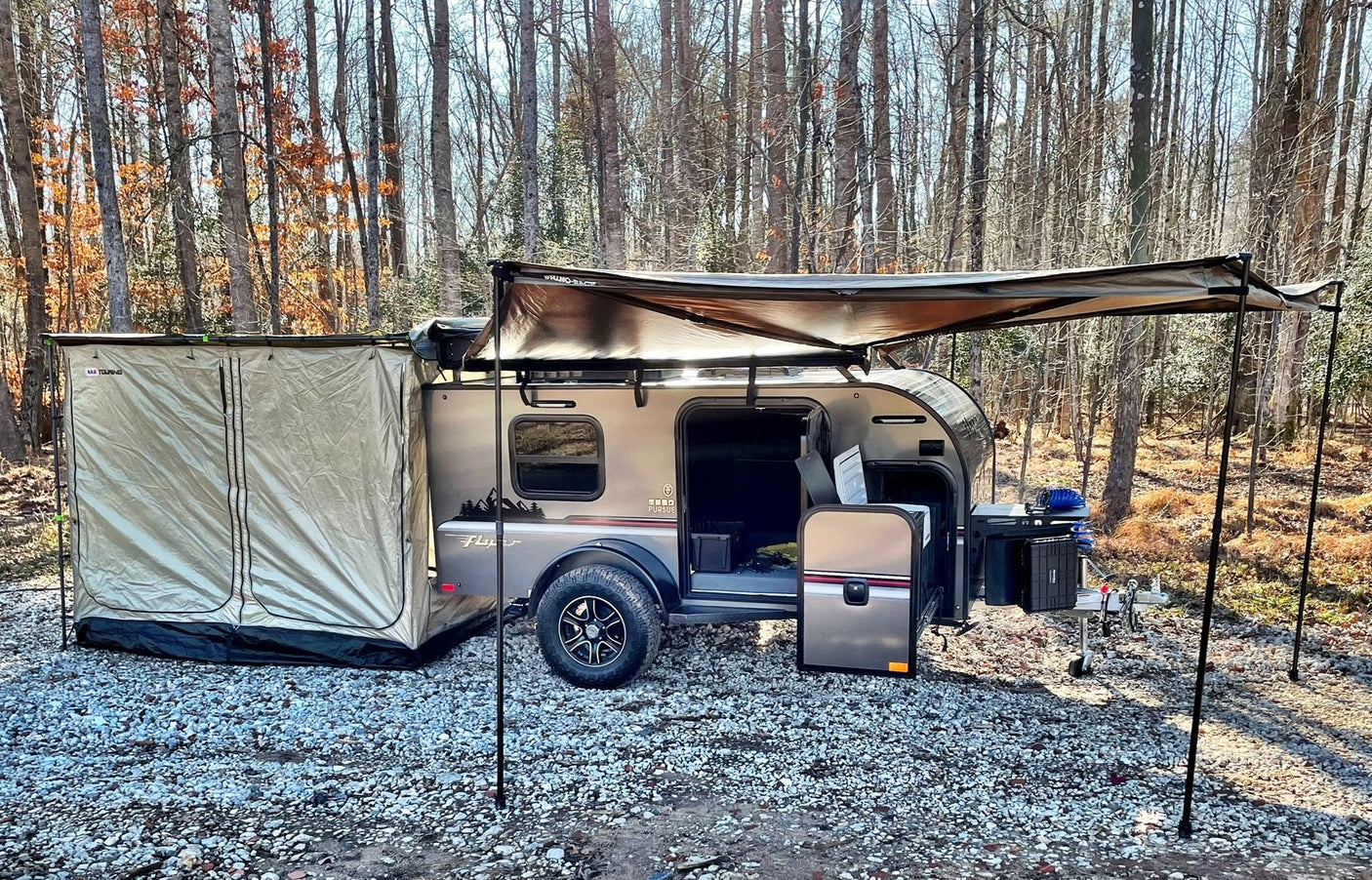 Explore nature with this RV rental setup: a teardrop camper with tent and awning at a wooded campsite.