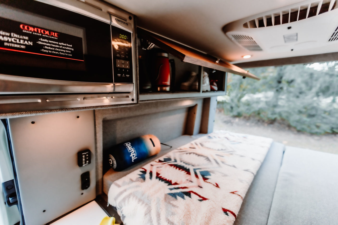 & blurred nature views from the window.|RV rental interior features a compact kitchen with a microwave